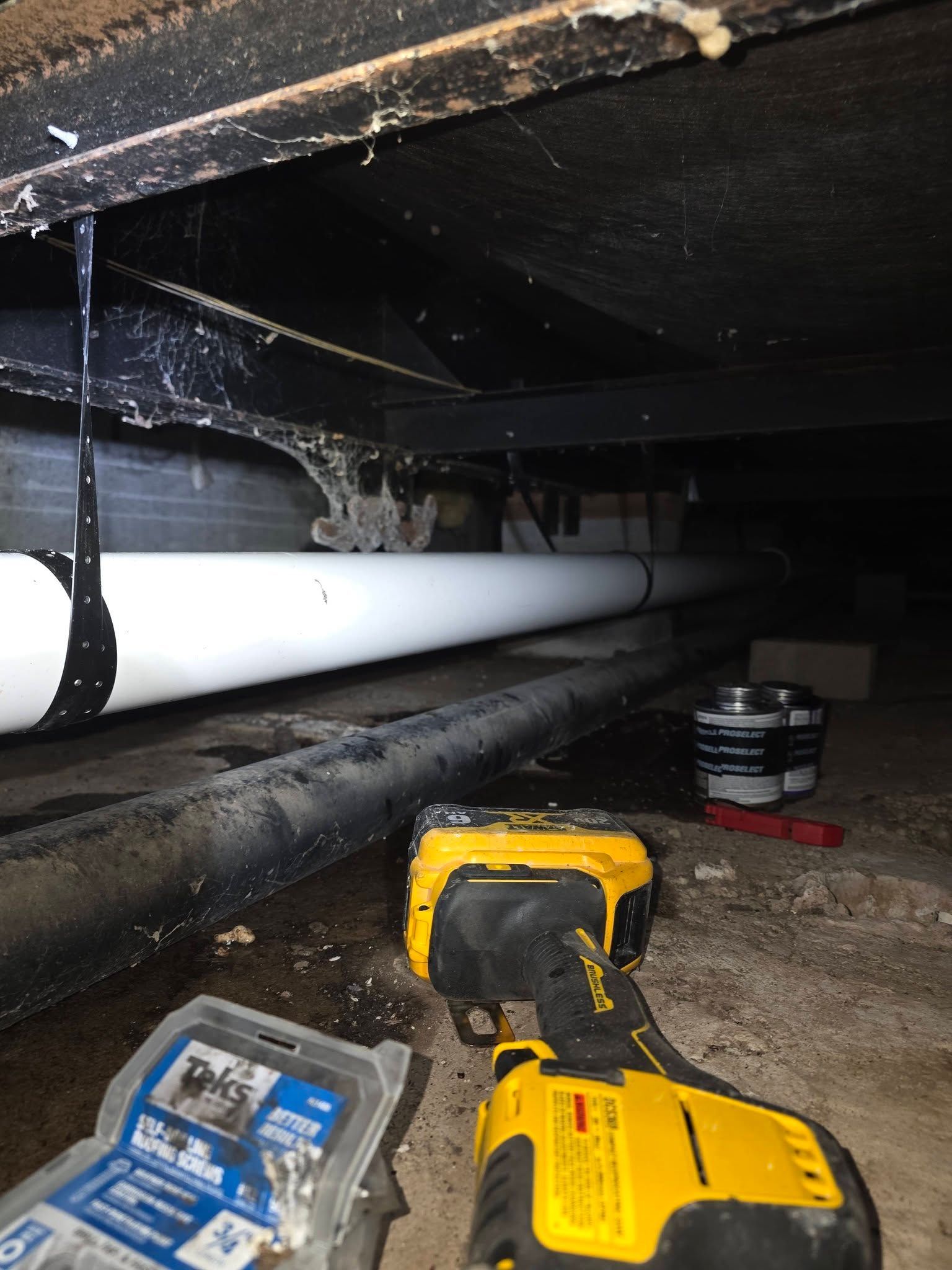 Under-floor crawlspace with pipes, tools, and water dripping from the ceiling