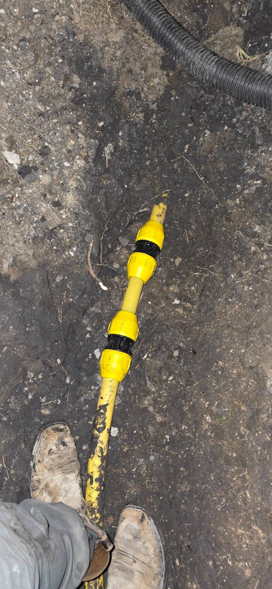 Yellow-and-black striped cable or marker on rough asphalt near a shoe.
