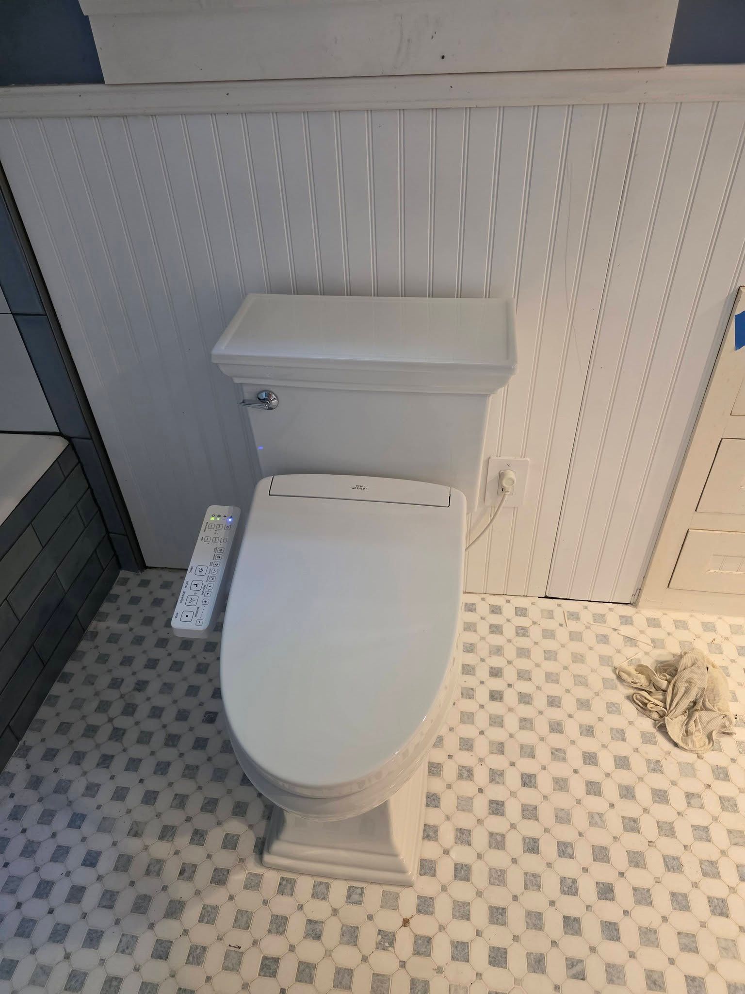 White toilet in a tiled bathroom stall with a small wall-mounted dispenser nearby