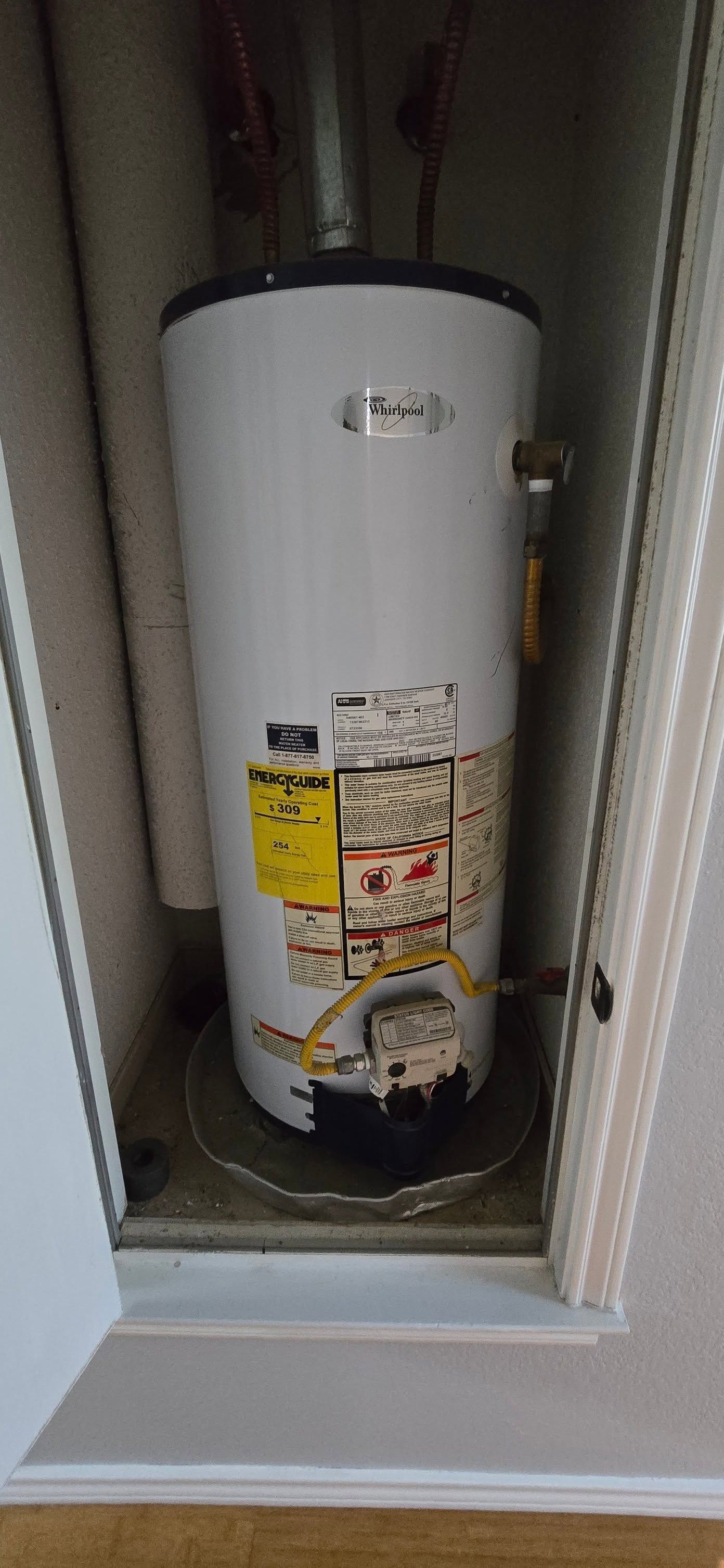Water heater in a closet alcove, with warning labels and plumbing visible.