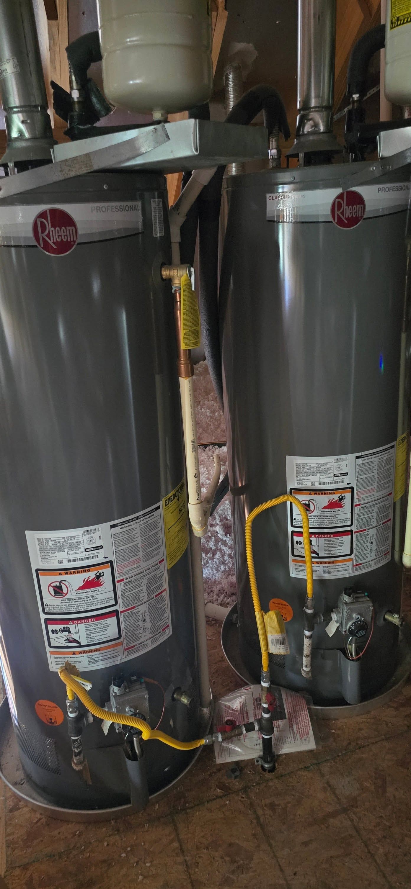 Two large silver water heaters with yellow gas lines in a utility room