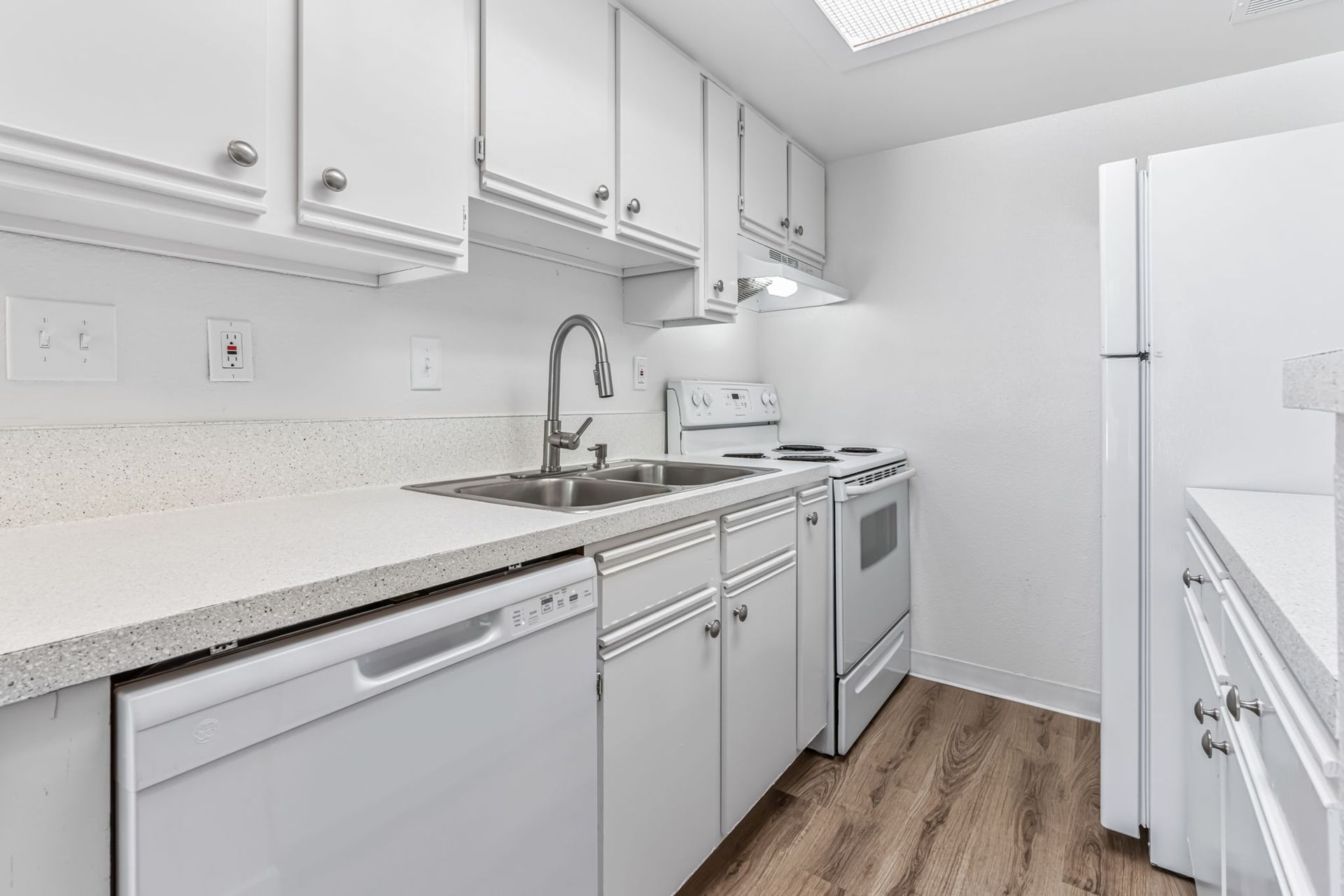 White kitchen with countertops, cabinets, appliances, sink, and wood-look flooring.