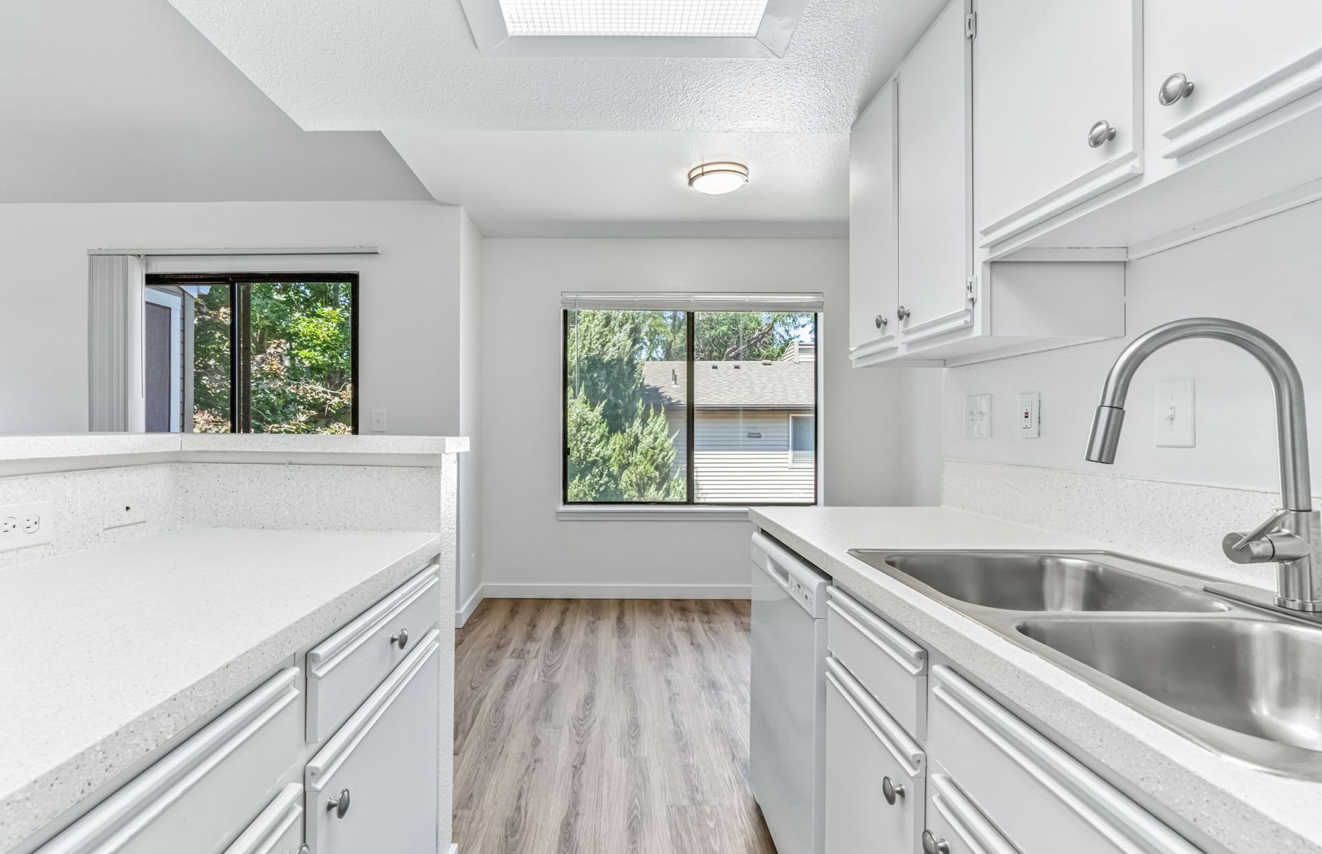 Bright kitchen with white cabinets, countertops, and a stainless steel sink, near a window with a view.