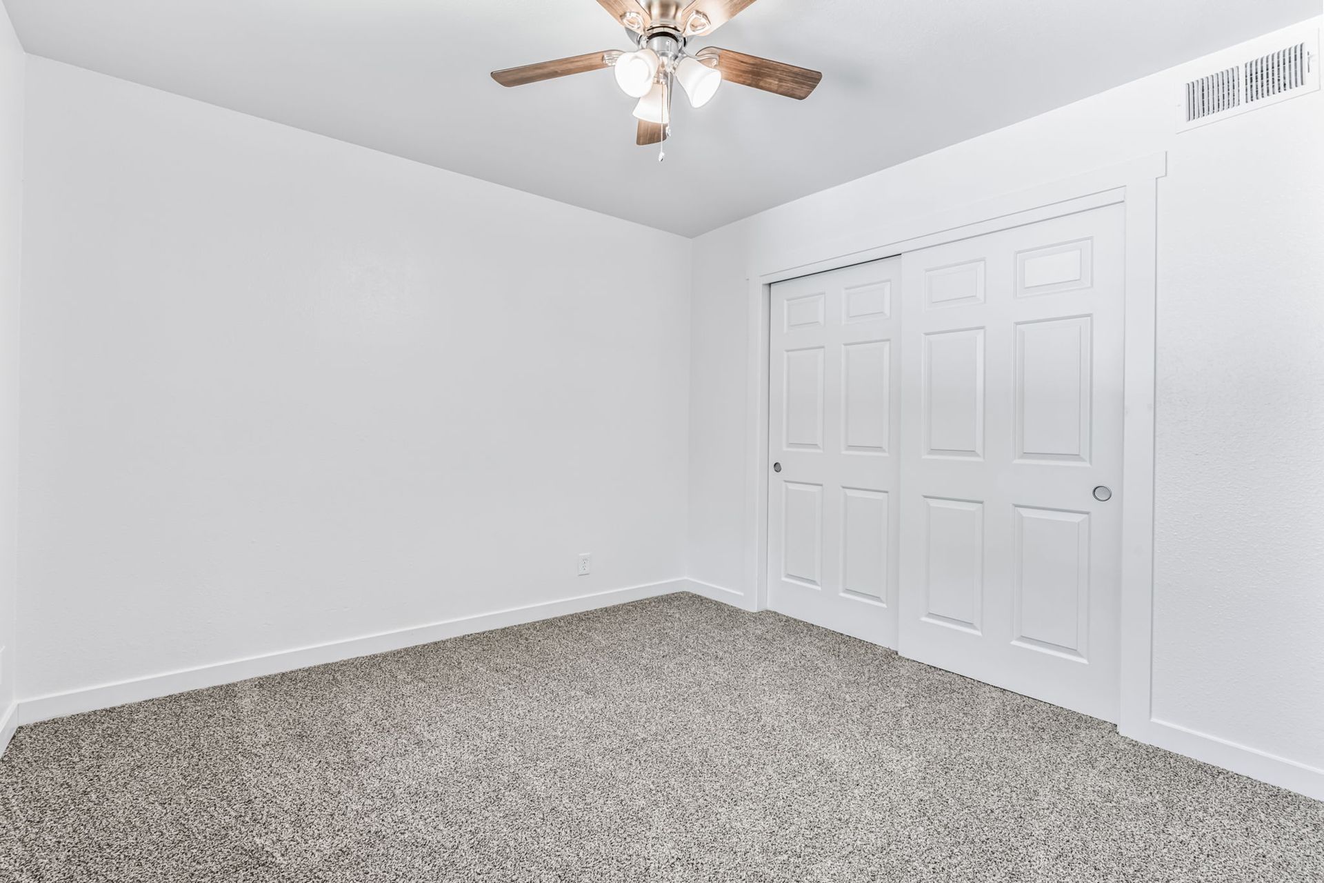 Empty bedroom with white walls, carpeted floor, sliding closet doors, and a ceiling fan.