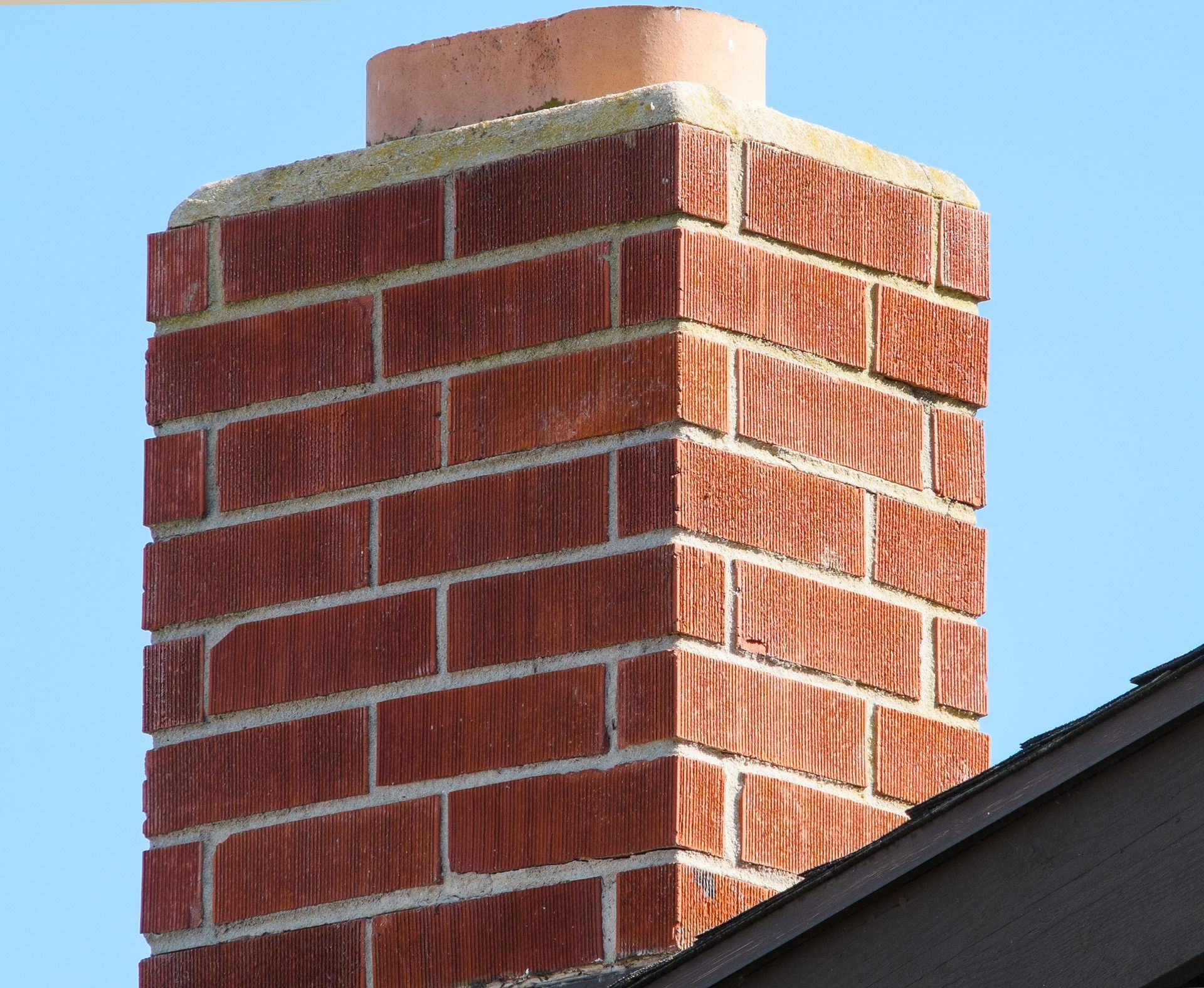 A brick chimney on top of a brick building with a blue sky in the background.