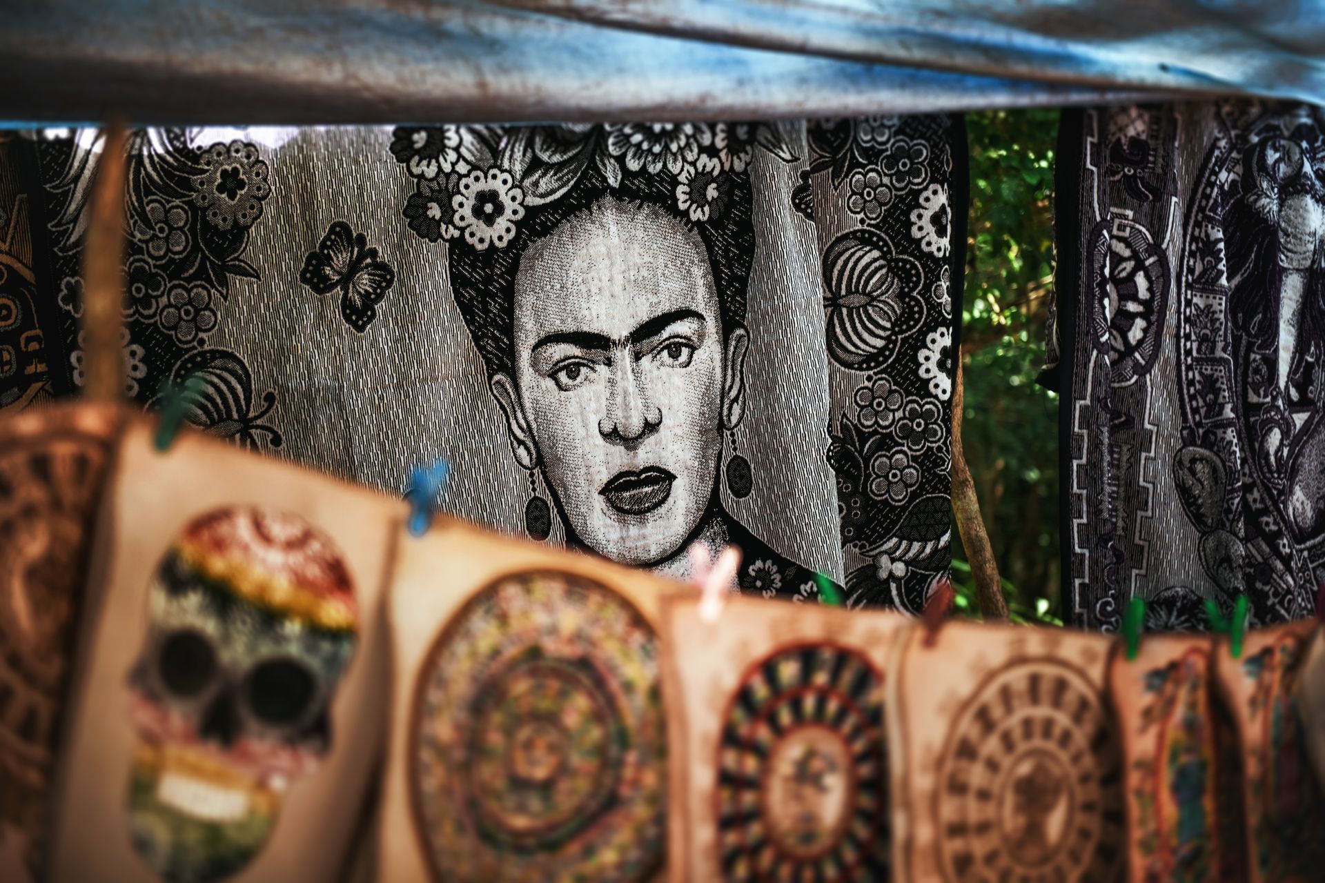 Retrato de Frida Kahlo detrás de coloridos artículos decorativos colgados en un mercado al aire libre.