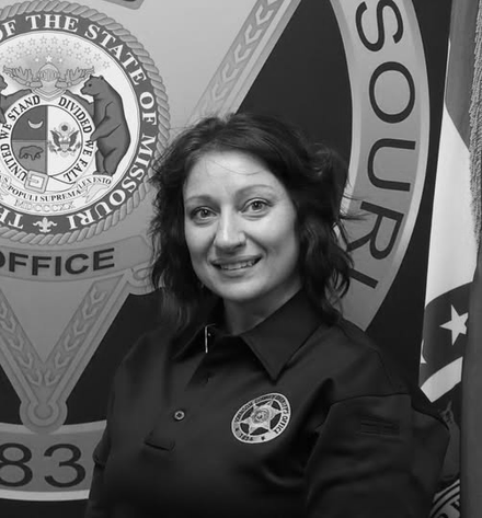 Woman in a dark uniform smiling in front of a Missouri State Highway Patrol-style seal backdrop.