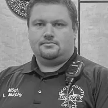 Sheriff's deputy in a dark polo shirt, facing the camera with a neutral expression.