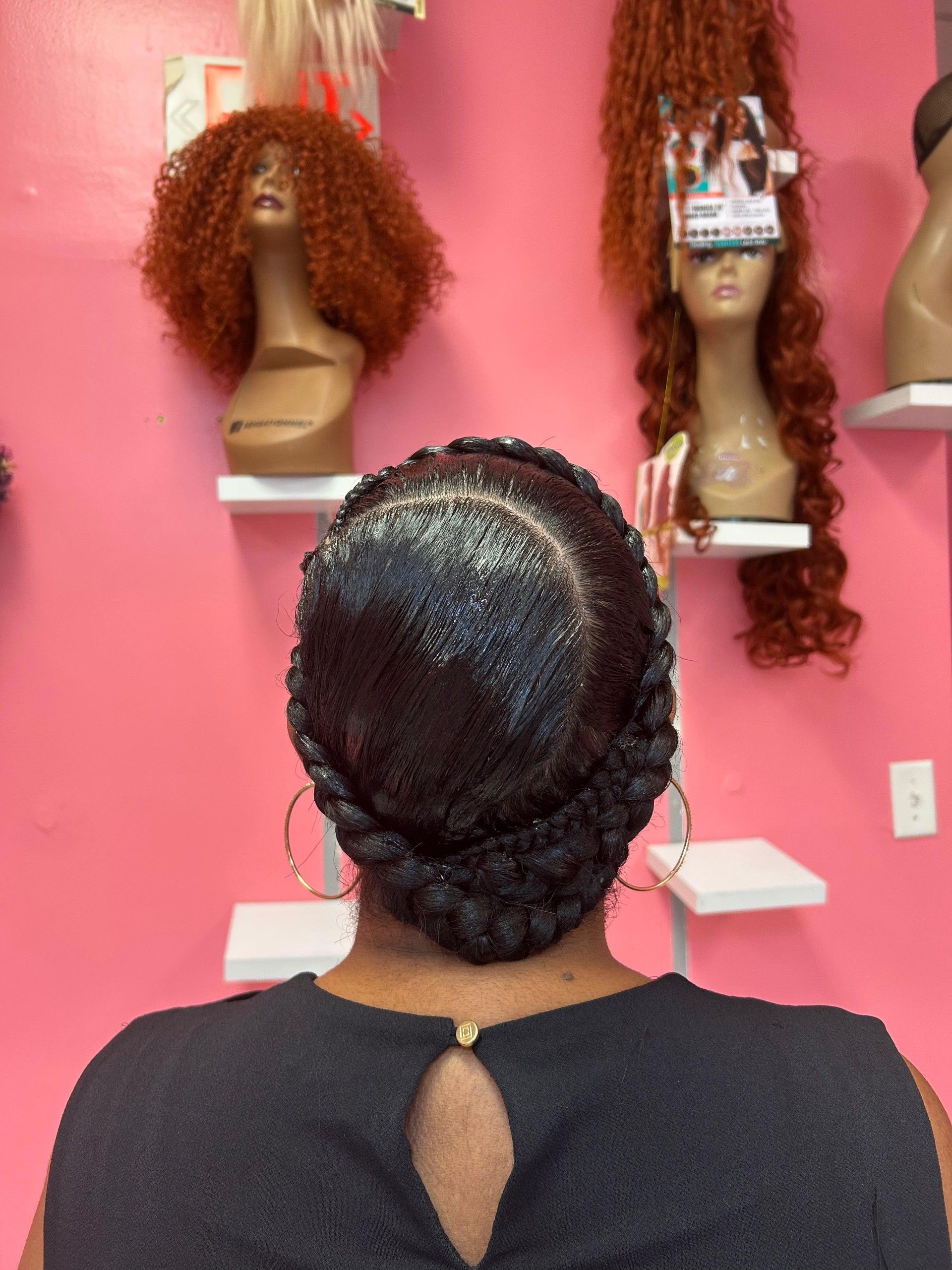 Person facing mannequin heads with wigs on a pink salon wall