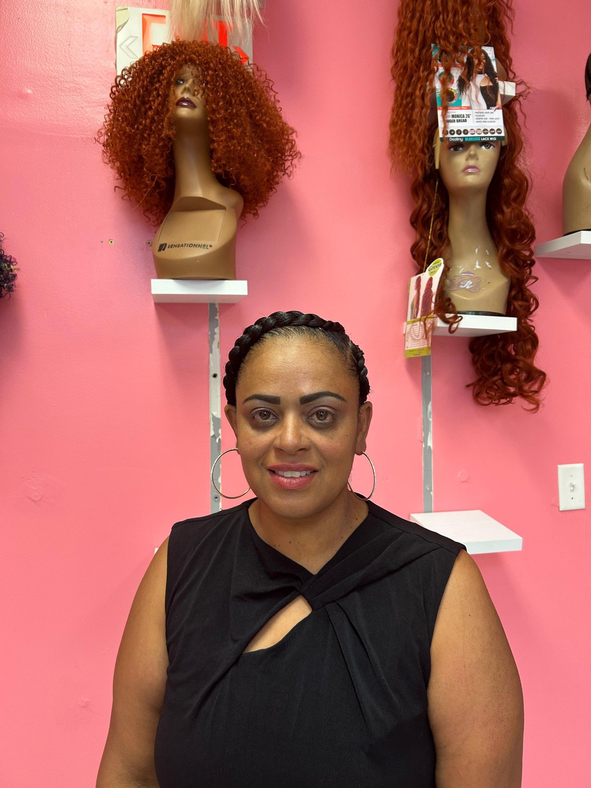 Person in black top standing in a pink room with mannequin heads and wigs on shelves.