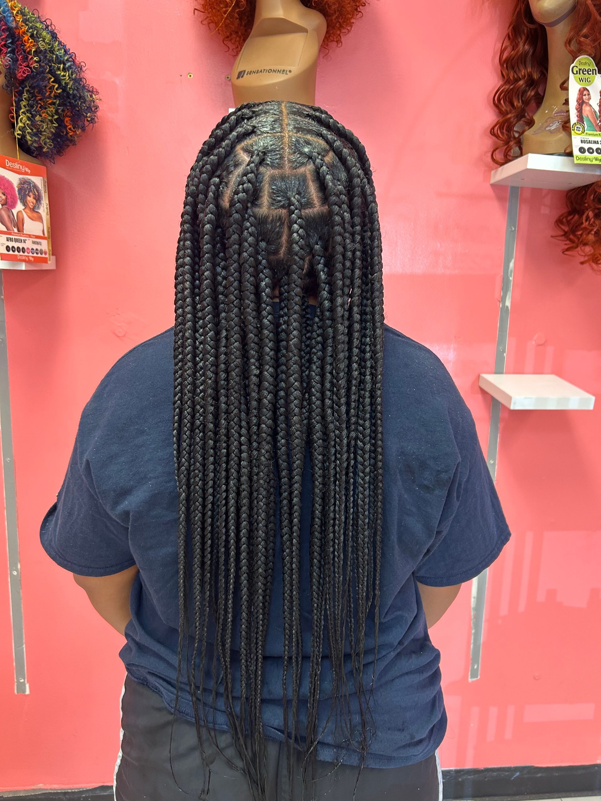 Person with long braided hair seen from behind, standing in a pink shop display area.