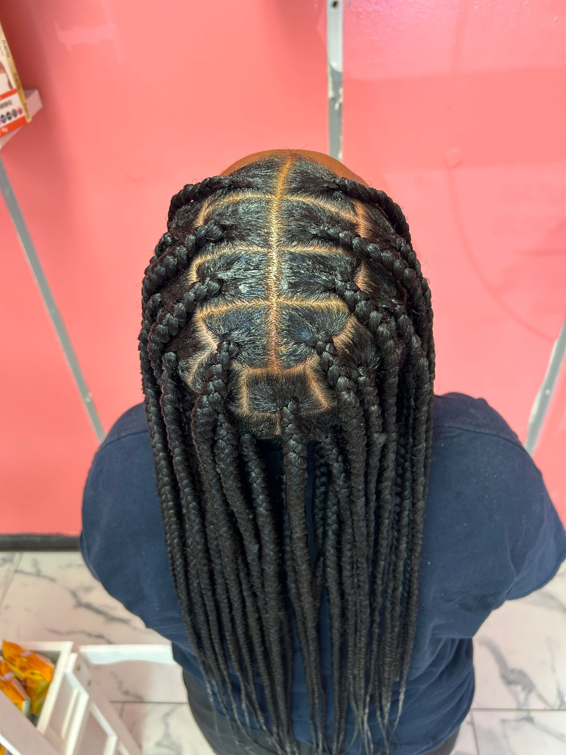 Top view of braided hairstyle with neat center part and gold accents against a pink background
