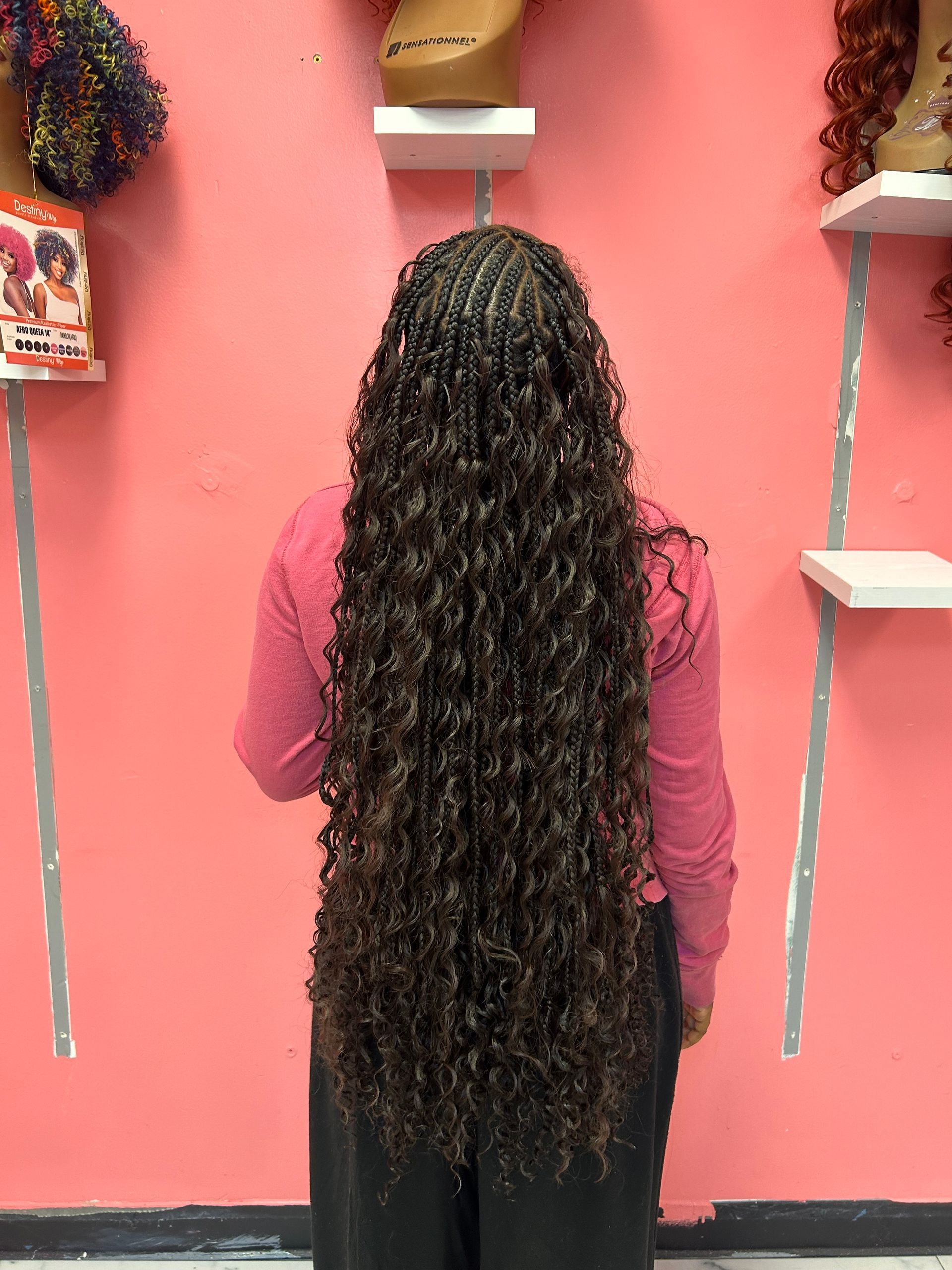 Person with long curly hair standing with back to camera in a pink room, framed by shelves on both sides