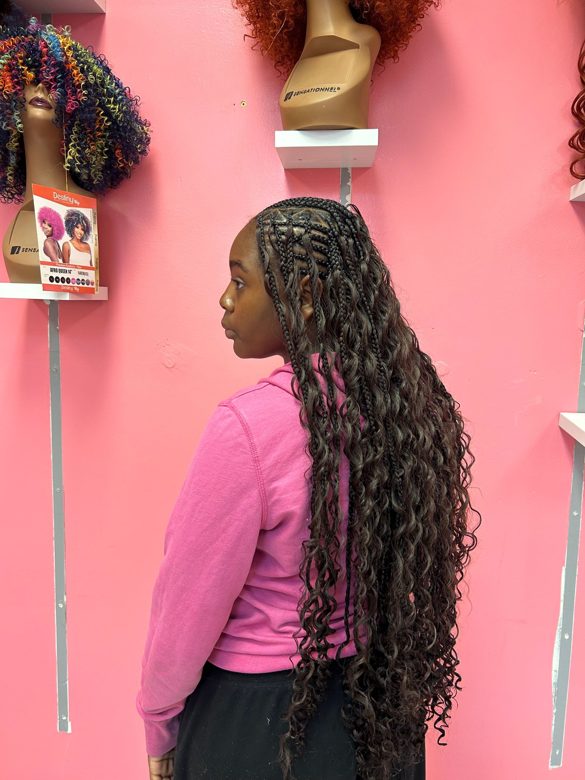 Woman with long curly hair in a pink top standing in profile against a pink wall display.