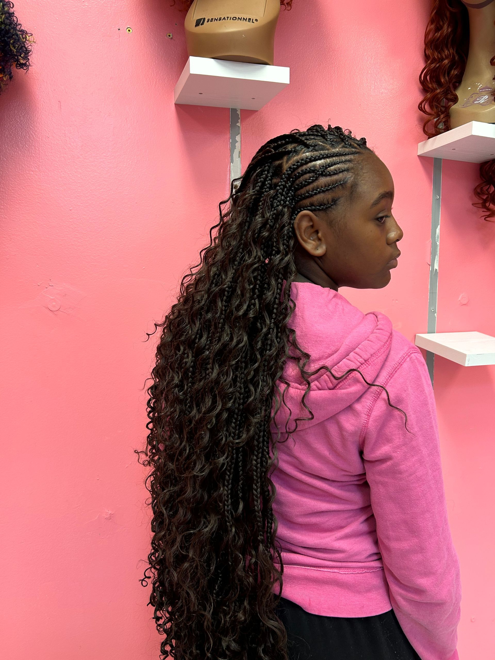 Side profile of a person in a pink sweater standing against a pink wall with shelves.