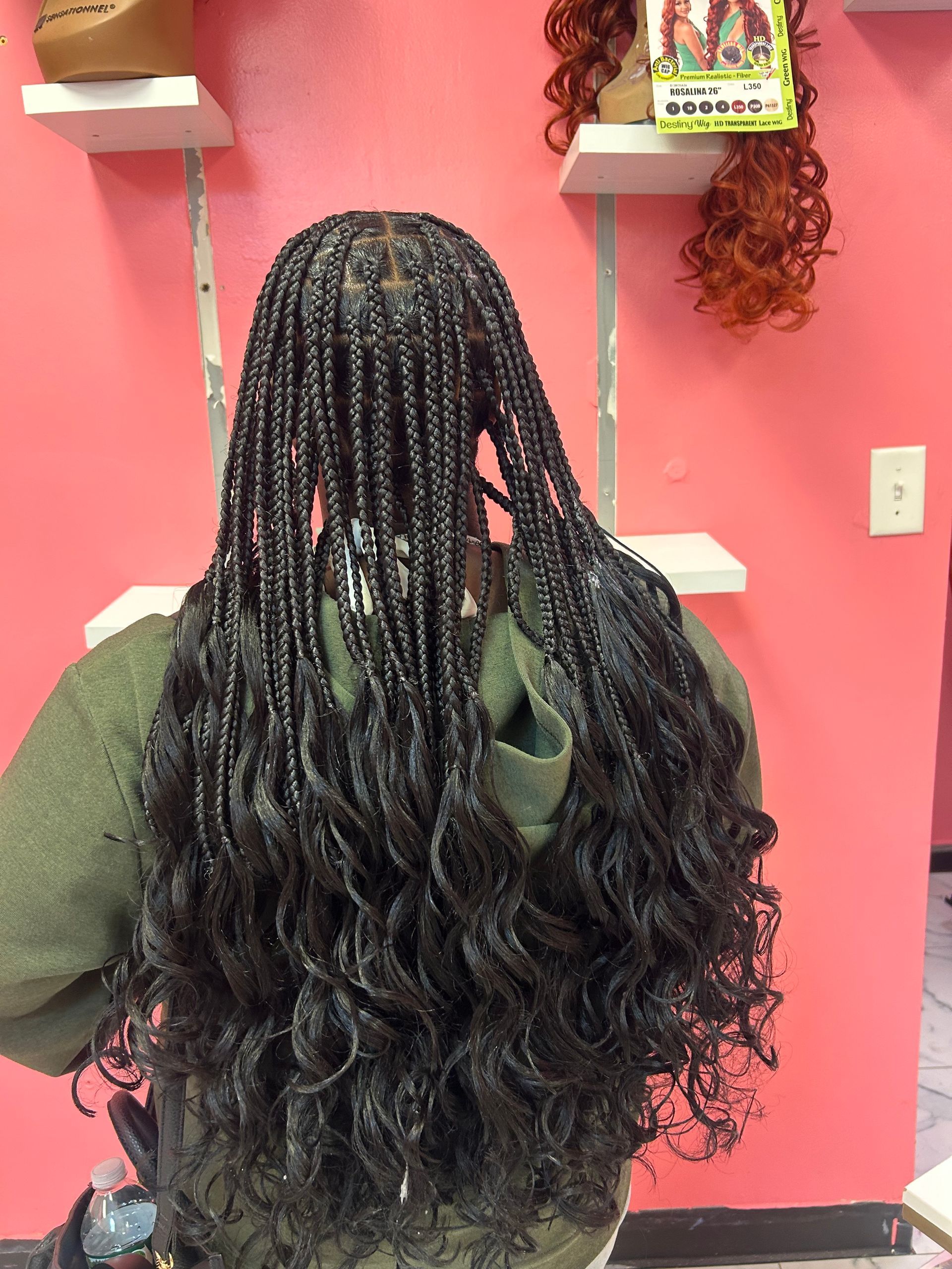 Braided hair extensions displayed on a mannequin against a pink wall with shelves