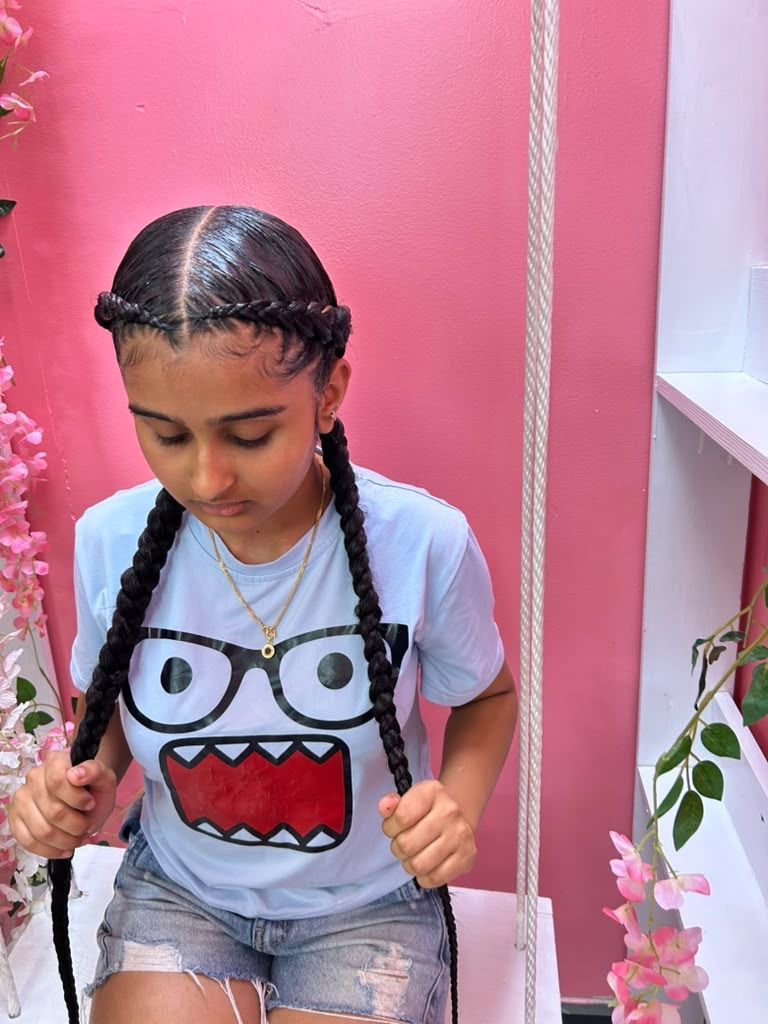 Young child with braided hair looking down, wearing a white cartoon T-shirt, in a pink room with flowers