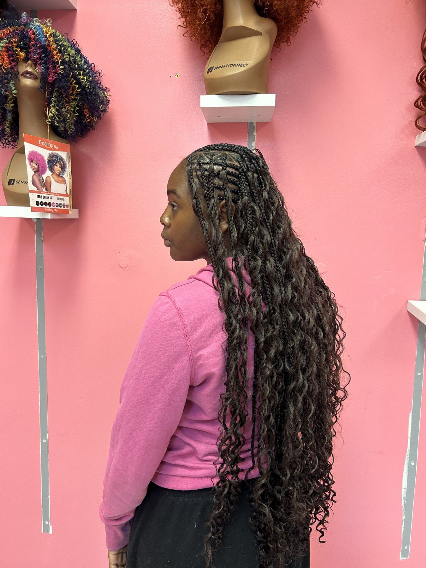 Woman with long curly hair standing in a pink salon, shown in profile.