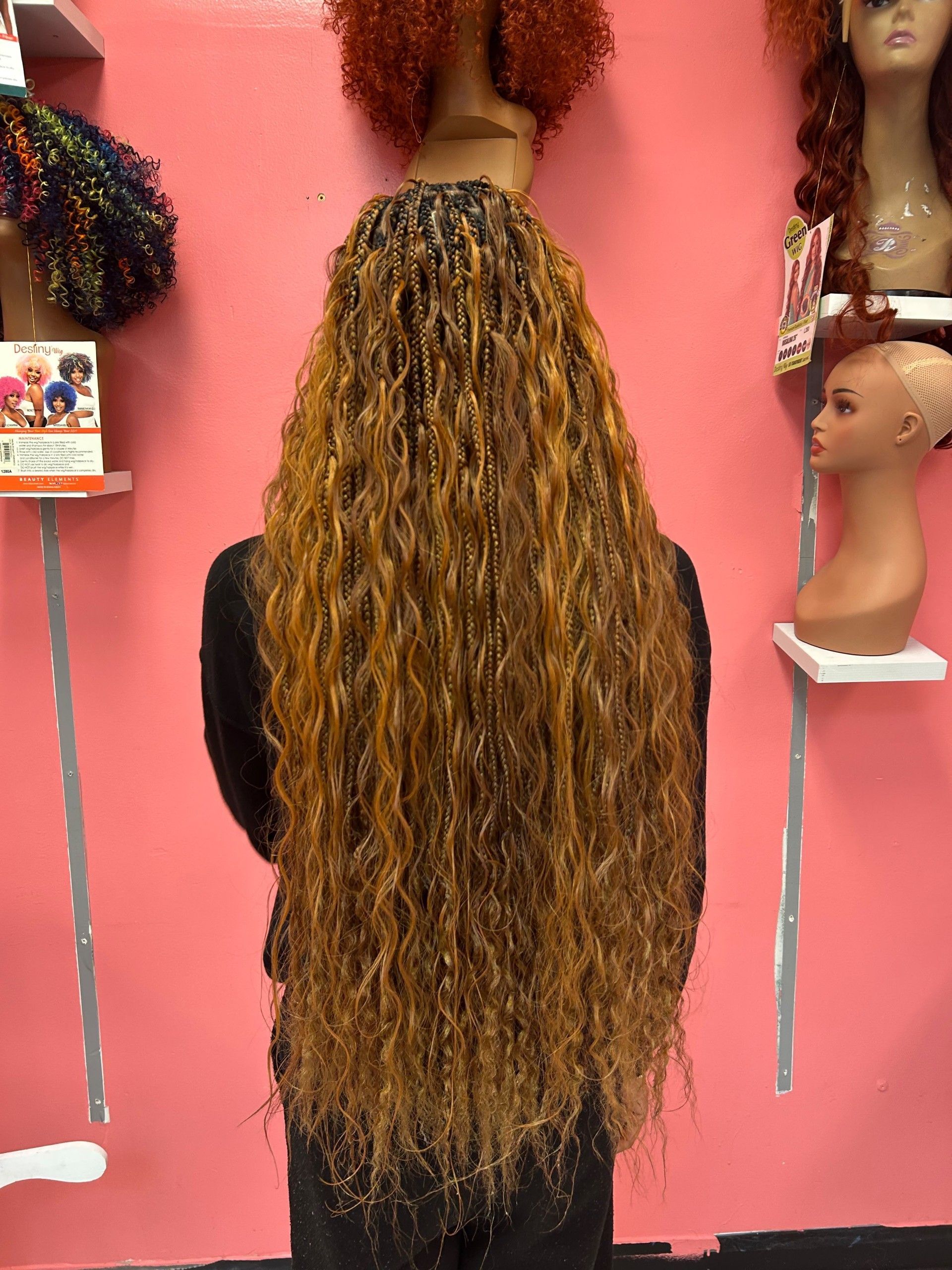 Long curly brown wig on a mannequin stand against a pink wall in a wig shop.