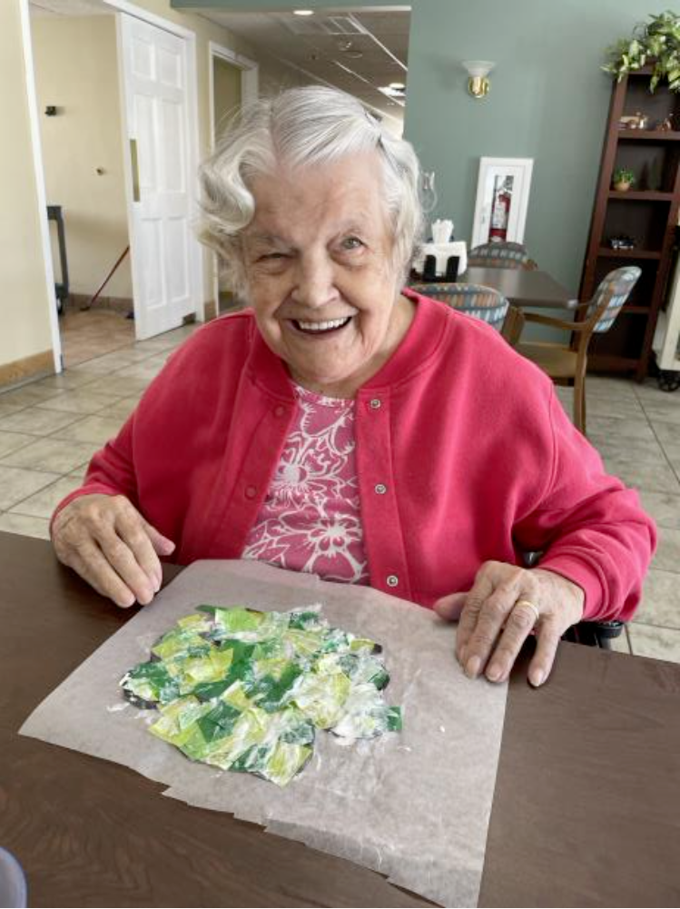 An elderly woman is sitting at a table with a piece of paper on it.