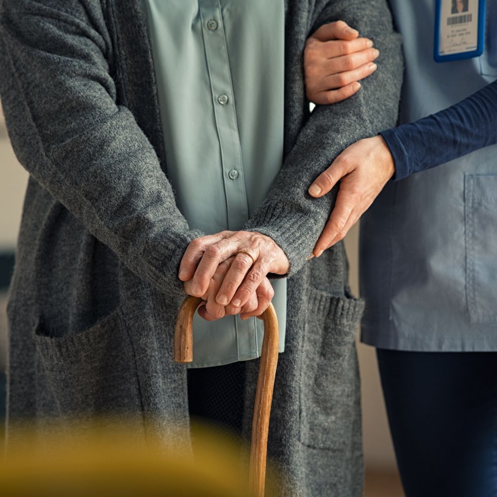 A nurse is helping an elderly woman with a cane.