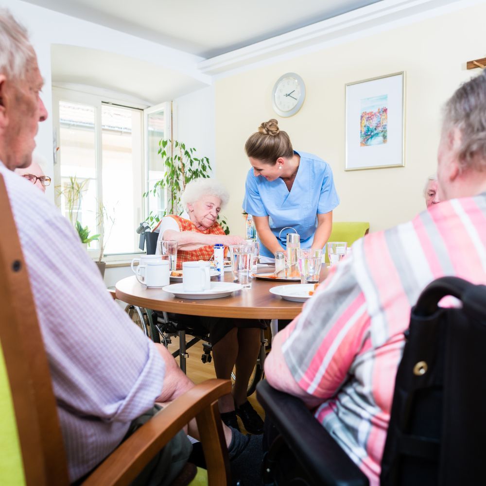 A group of people are sitting around a table with a nurse standing behind them