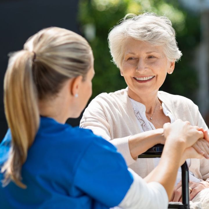 A woman in a blue shirt is talking to an older woman in a wheelchair