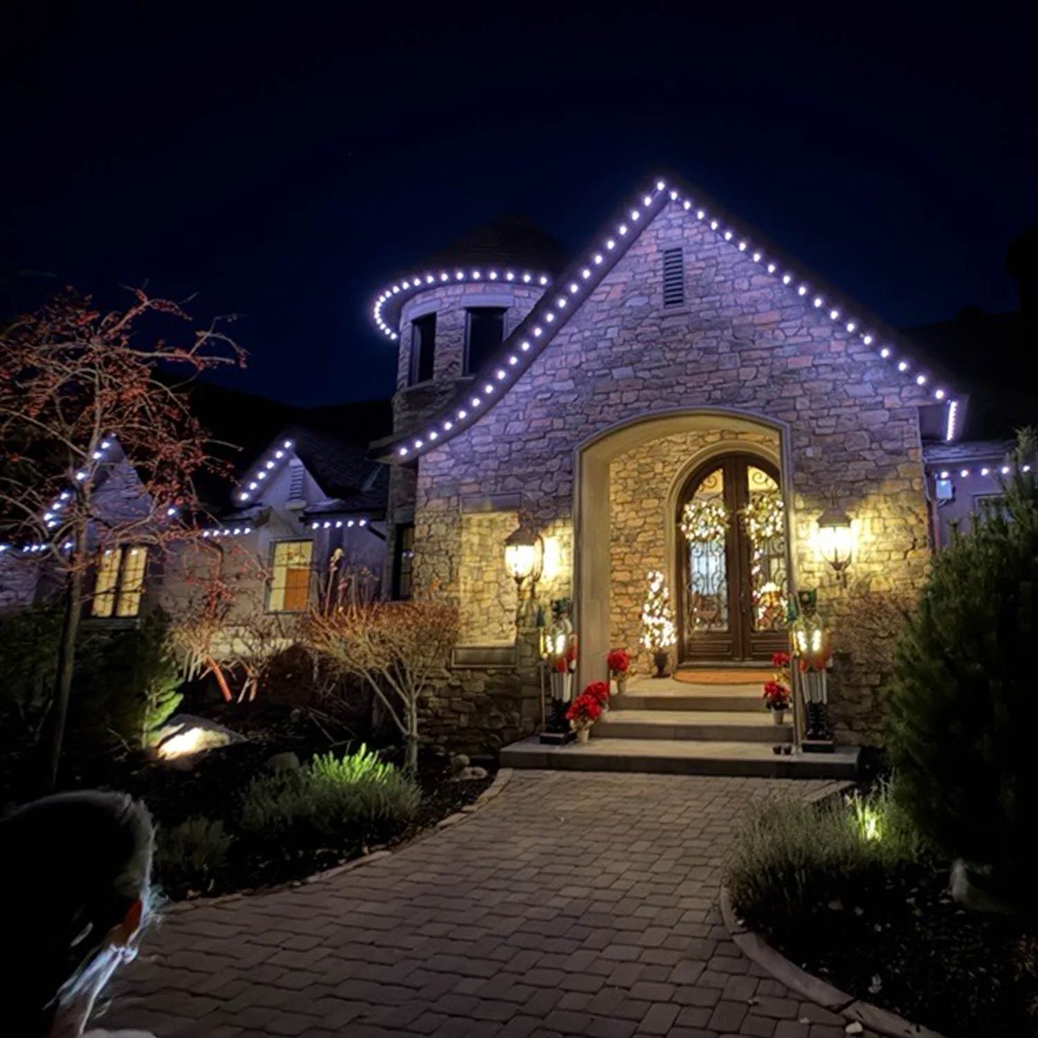 Stone house at night outlined with white lights, with a lit front door and walkway leading up to it