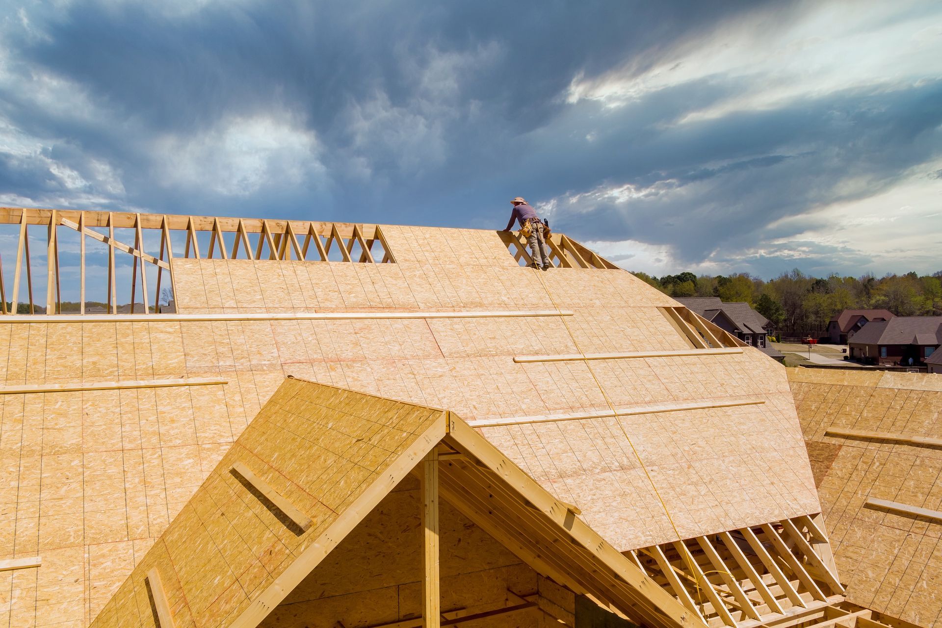 New Roof Installation - Phoenix Storm Restoration Construction workers installing plywood sheathing on a roof under a cloudy sky.