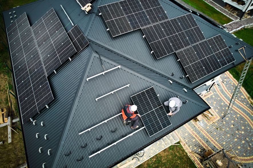 Solar Detach & Reinstall - Phoenix Storm Restoration Solar panels are being installed on a dark grey roof by two workers in safety gear.