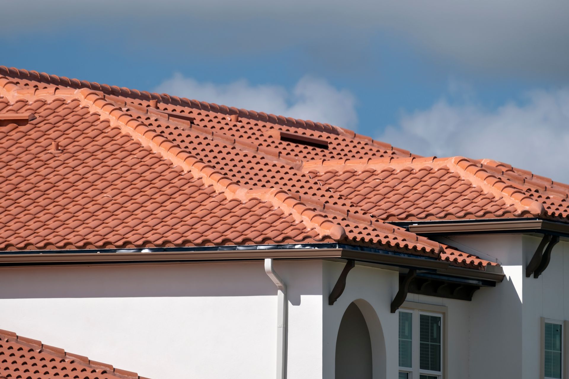 Clay tile roof on a white house against a blue sky.