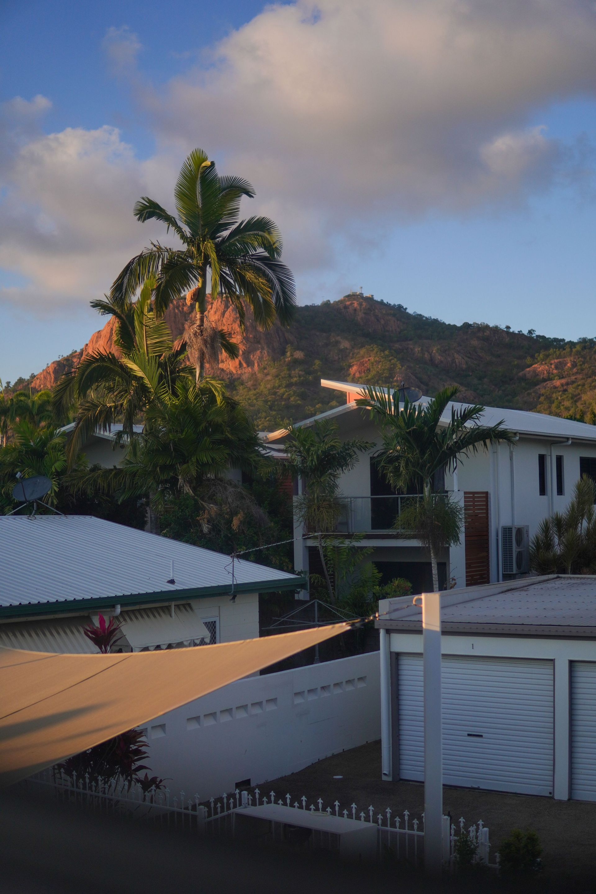 Mountain and palm trees behind houses at sunset under a cloudy sky