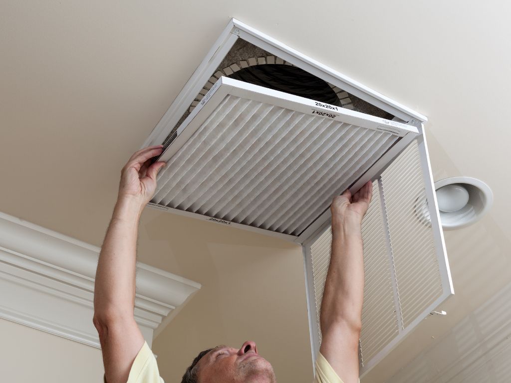 A man is cleaning a ceiling vent with a filter.
