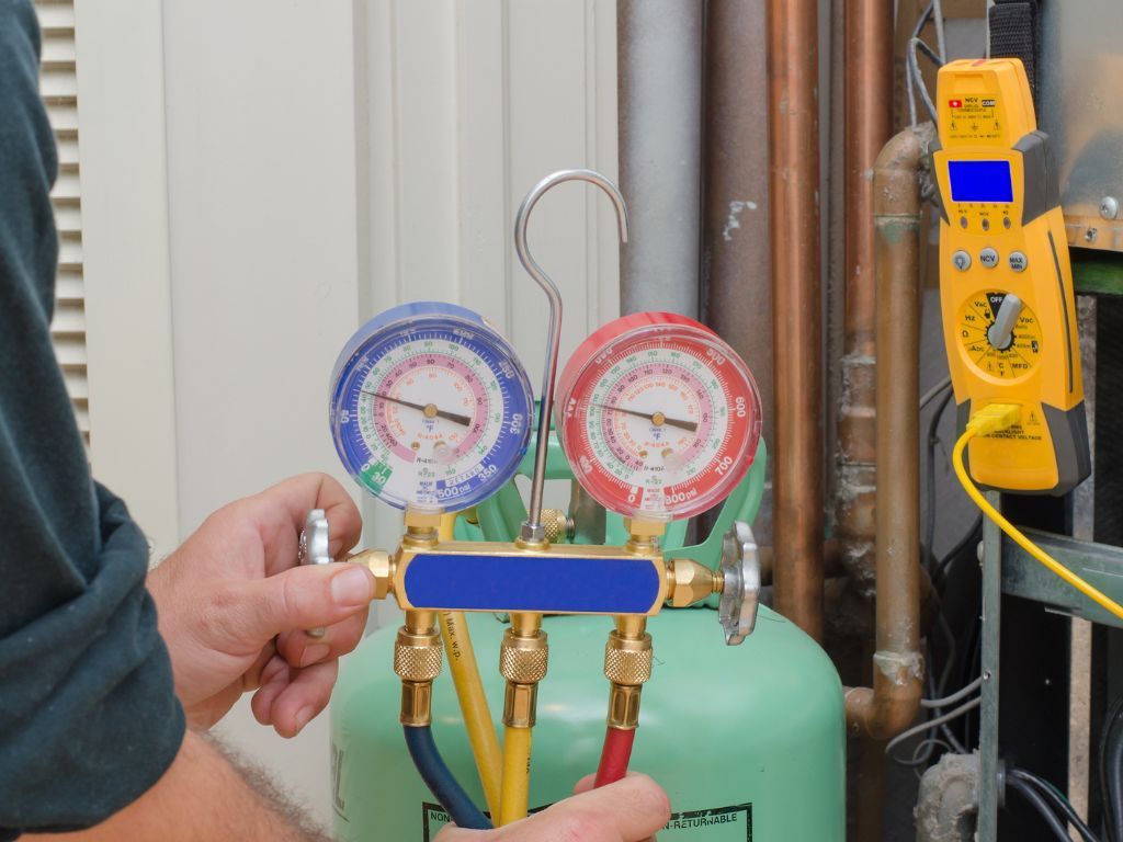 A man is holding a gauge in front of a refrigerant tank.