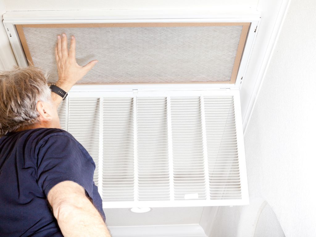 A man is cleaning an air filter on the ceiling of a room.