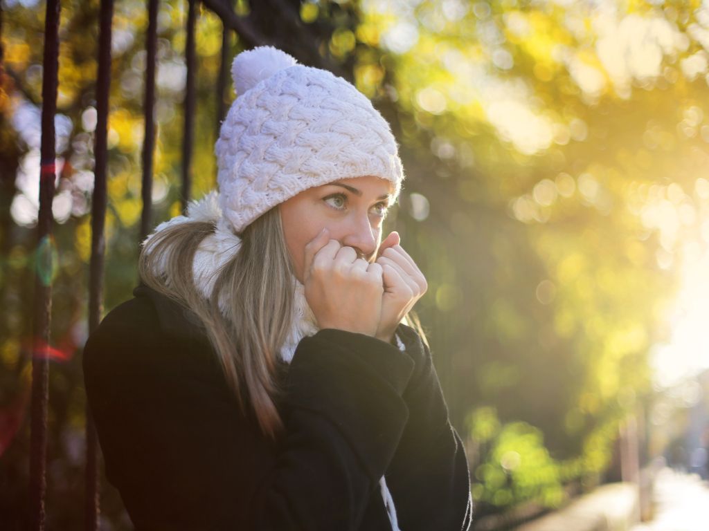 A woman wearing a white hat and scarf is sitting on a railing.