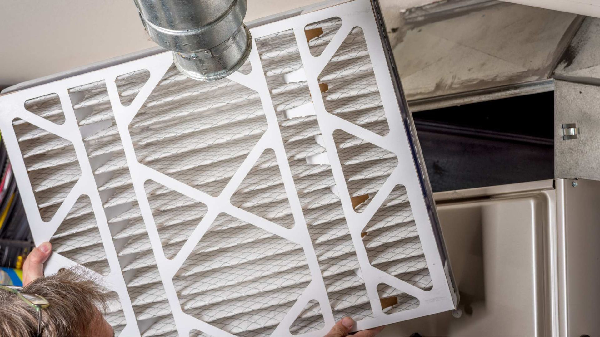 Dirty white air filter being removed from an HVAC vent with ductwork visible behind it