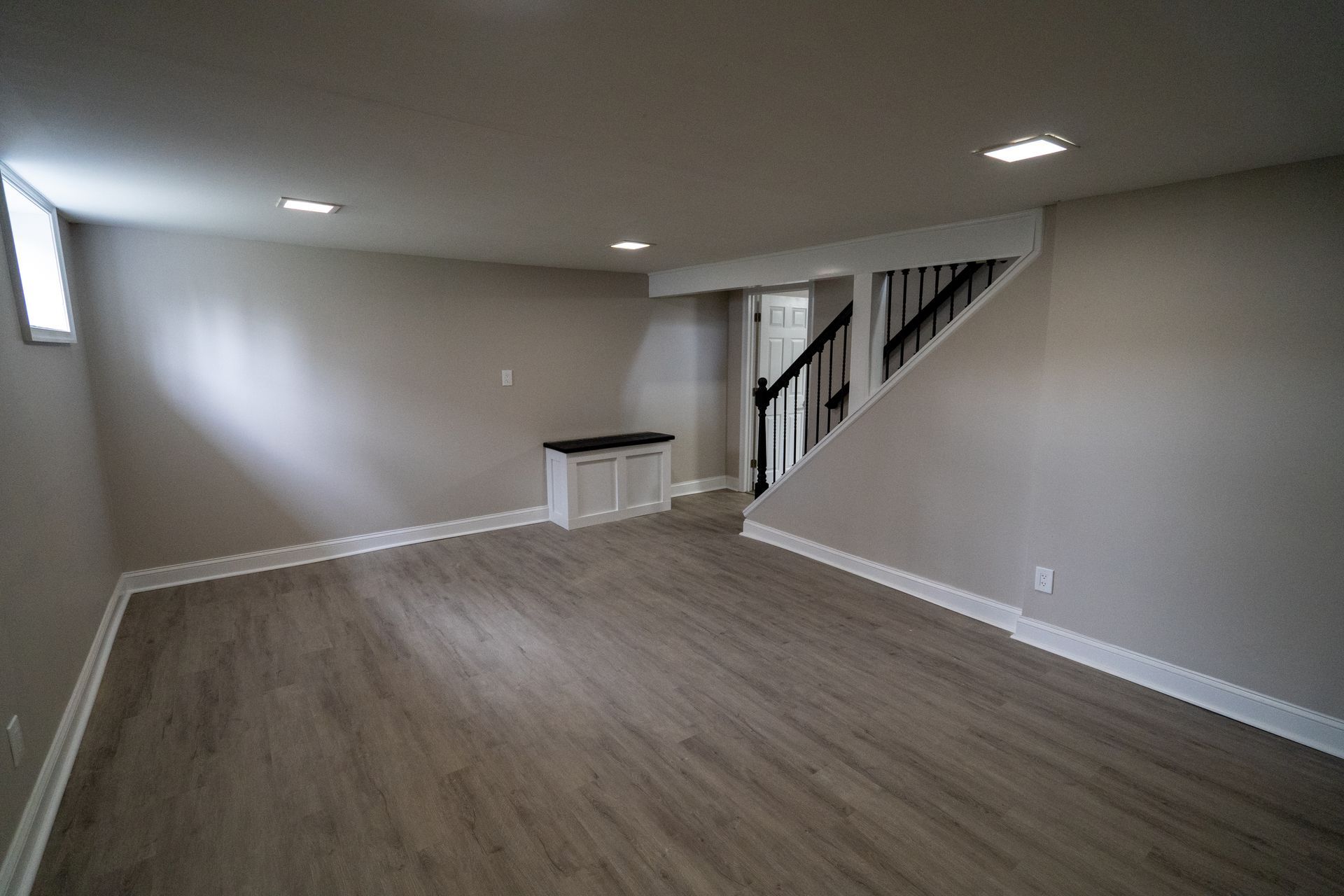 Empty finished basement living area with wood floors, recessed lights, and staircase along the right wall