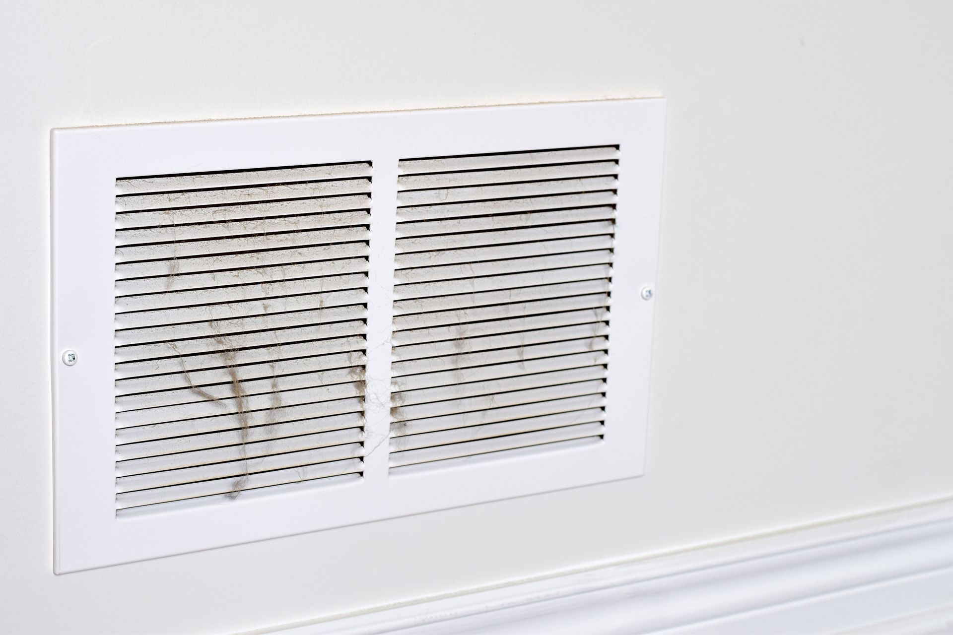 White wall vent cover with slatted openings and visible dust or rust stains.