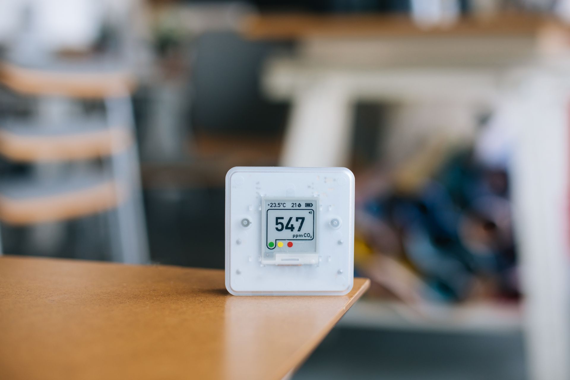 A white air quality monitor displaying 547 ppm sits on a wooden table in a blurred indoor setting.