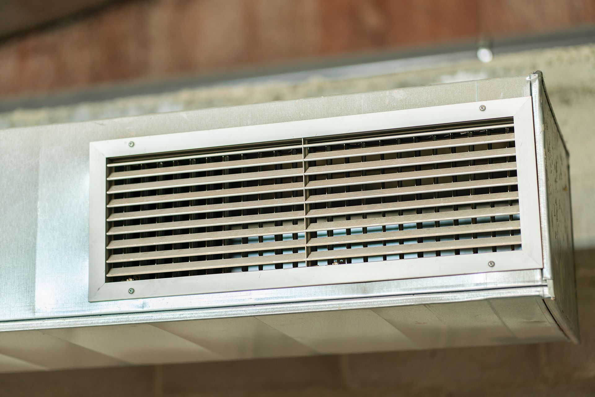 Metal air vent in a ceiling, with horizontal louvers, attached to ductwork.