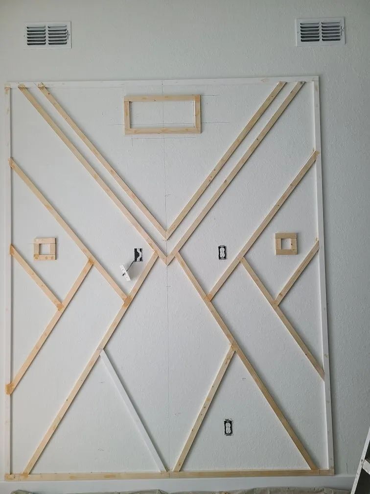 White wall with gold geometric trim forming an abstract diamond pattern and small vents at the top.