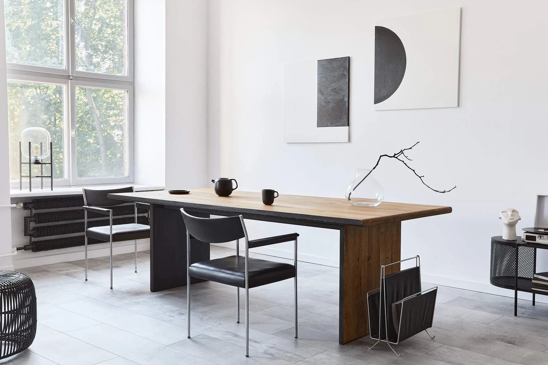 Minimalist home office with wooden desk, black chair, and large windows in a bright room