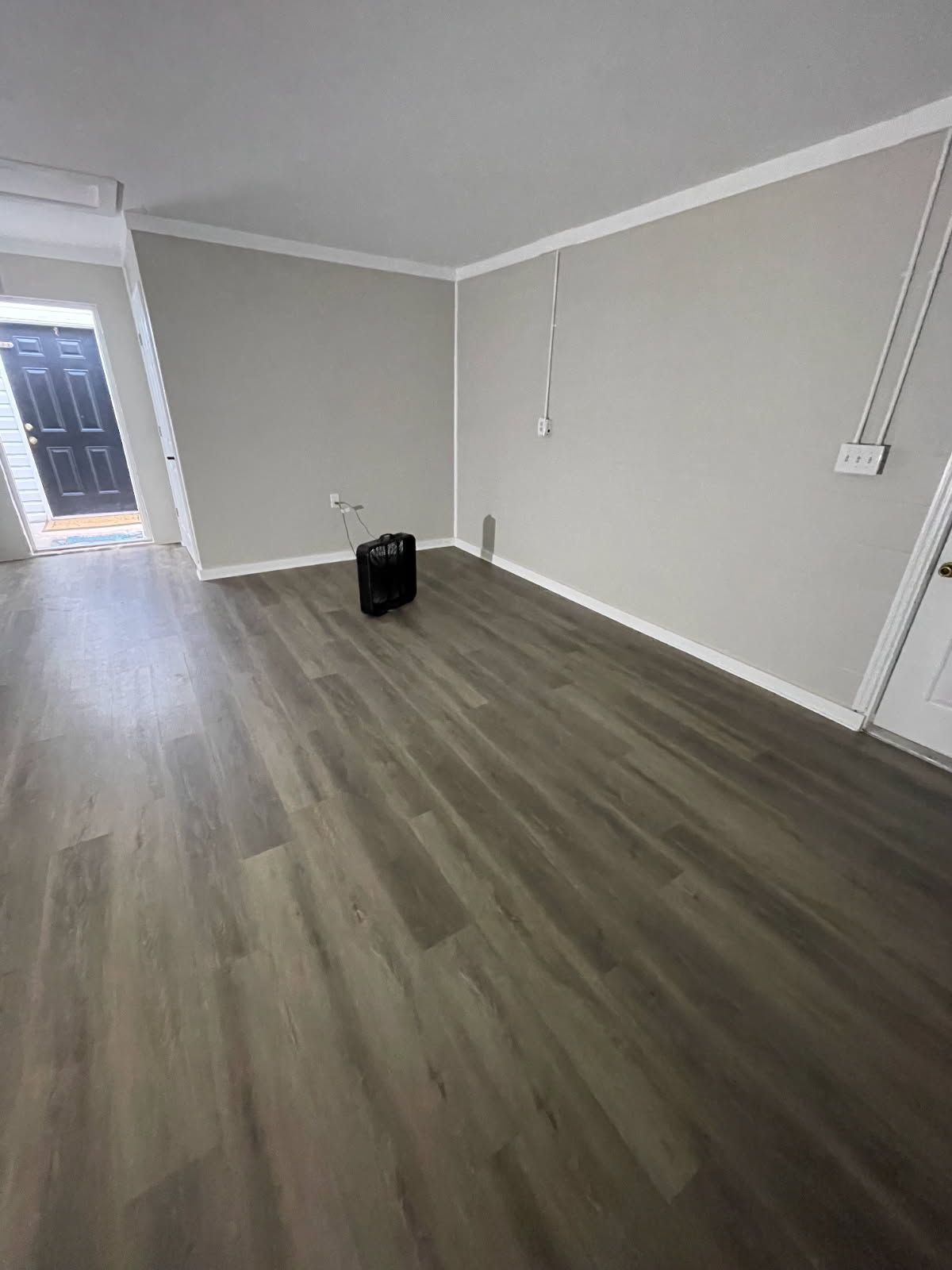 Empty living room with gray wood floors, beige walls, and a black bag near the center.