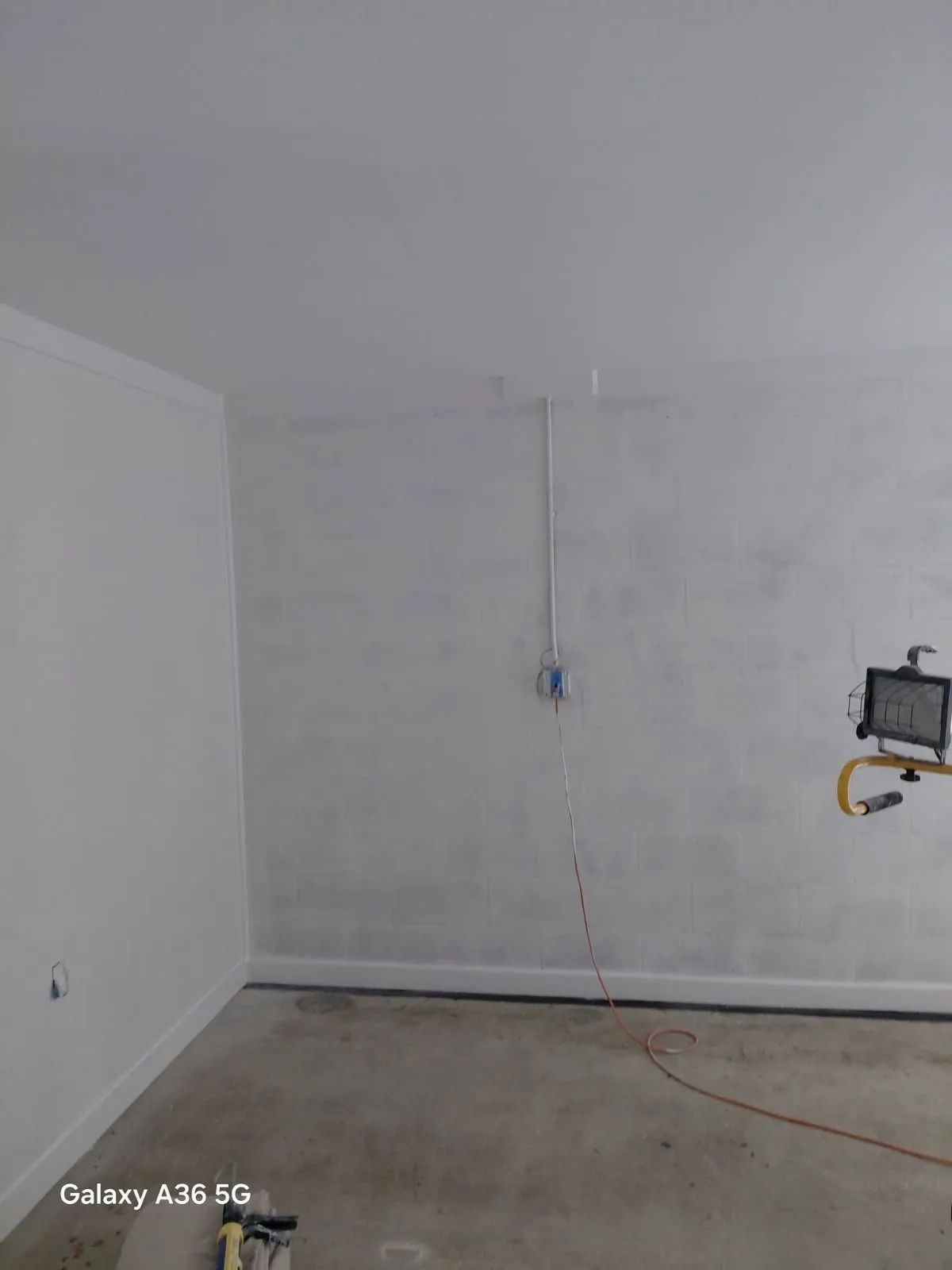 Empty white room with unfinished walls, concrete floor, and a wall-mounted work light on the right.