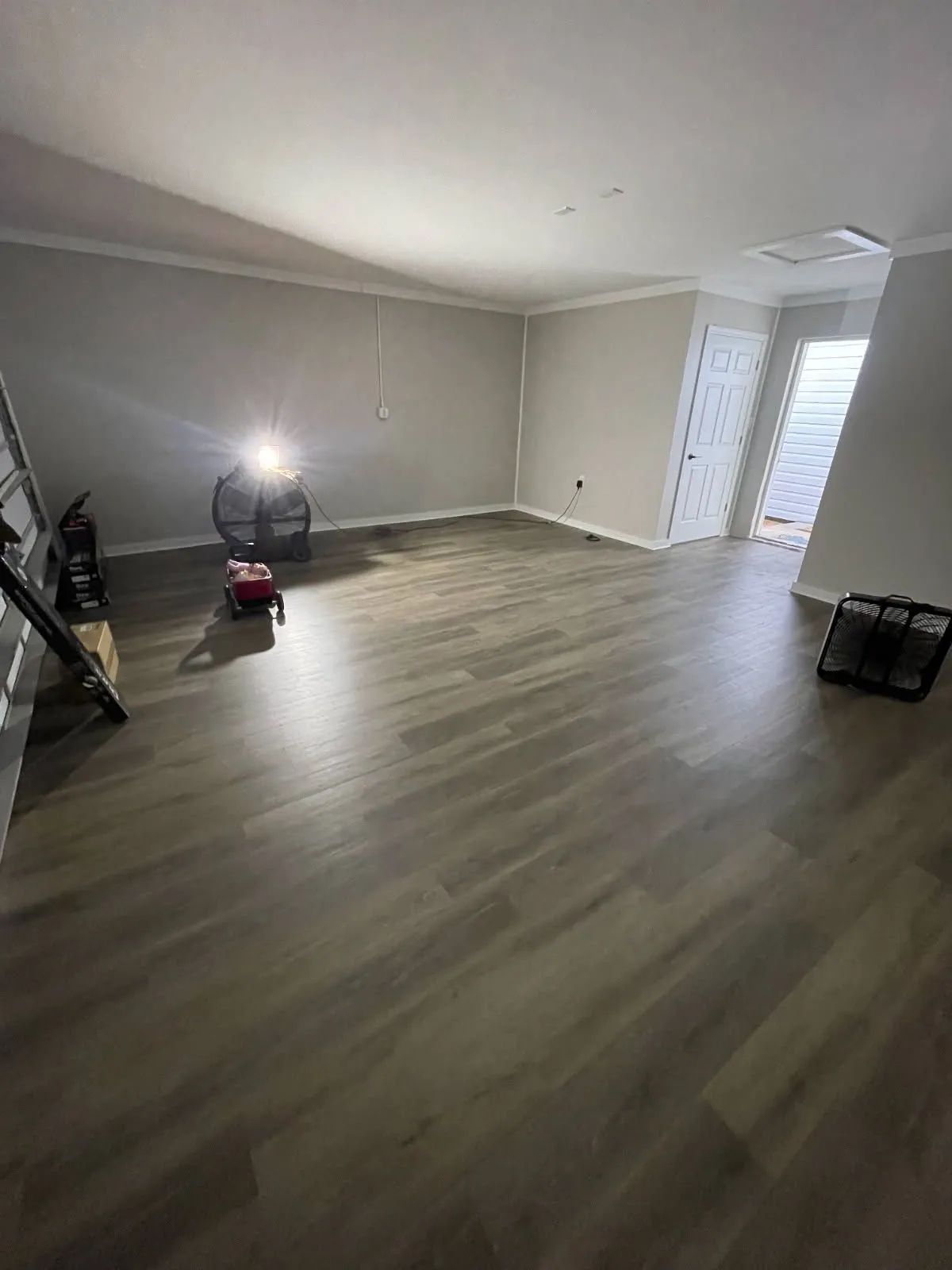 Empty room with gray wood floors, recessed lighting, and a bright doorway at the far end.