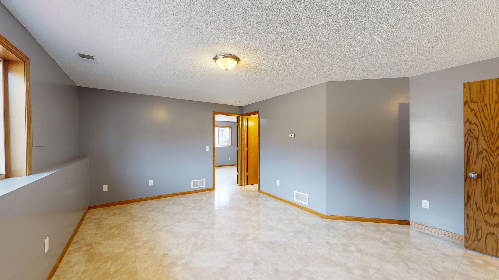 Empty beige living room with tiled floor, windows, and an open doorway to a hall