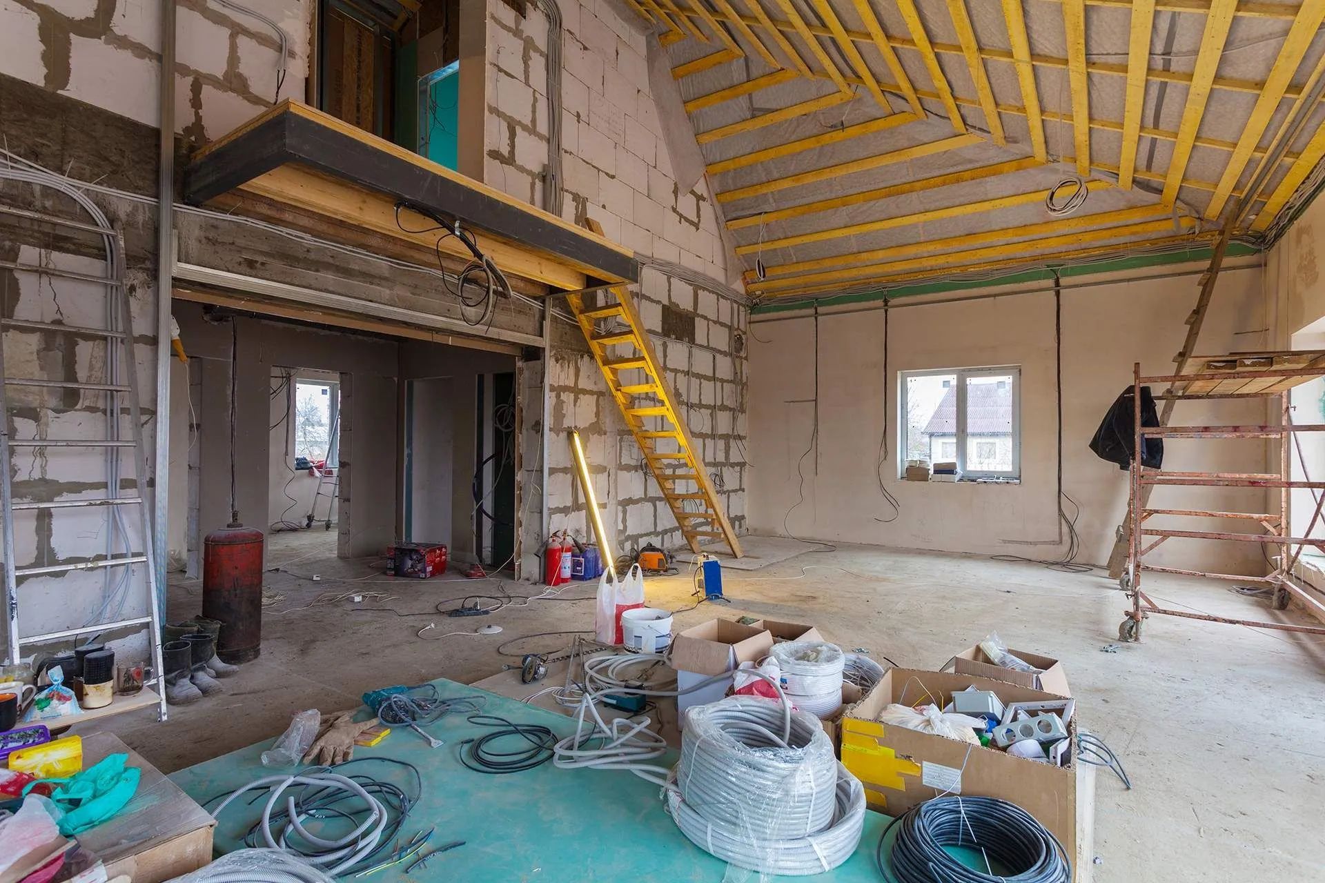 Renovation site with exposed ceiling, ladder, tools, and construction materials scattered across the floor