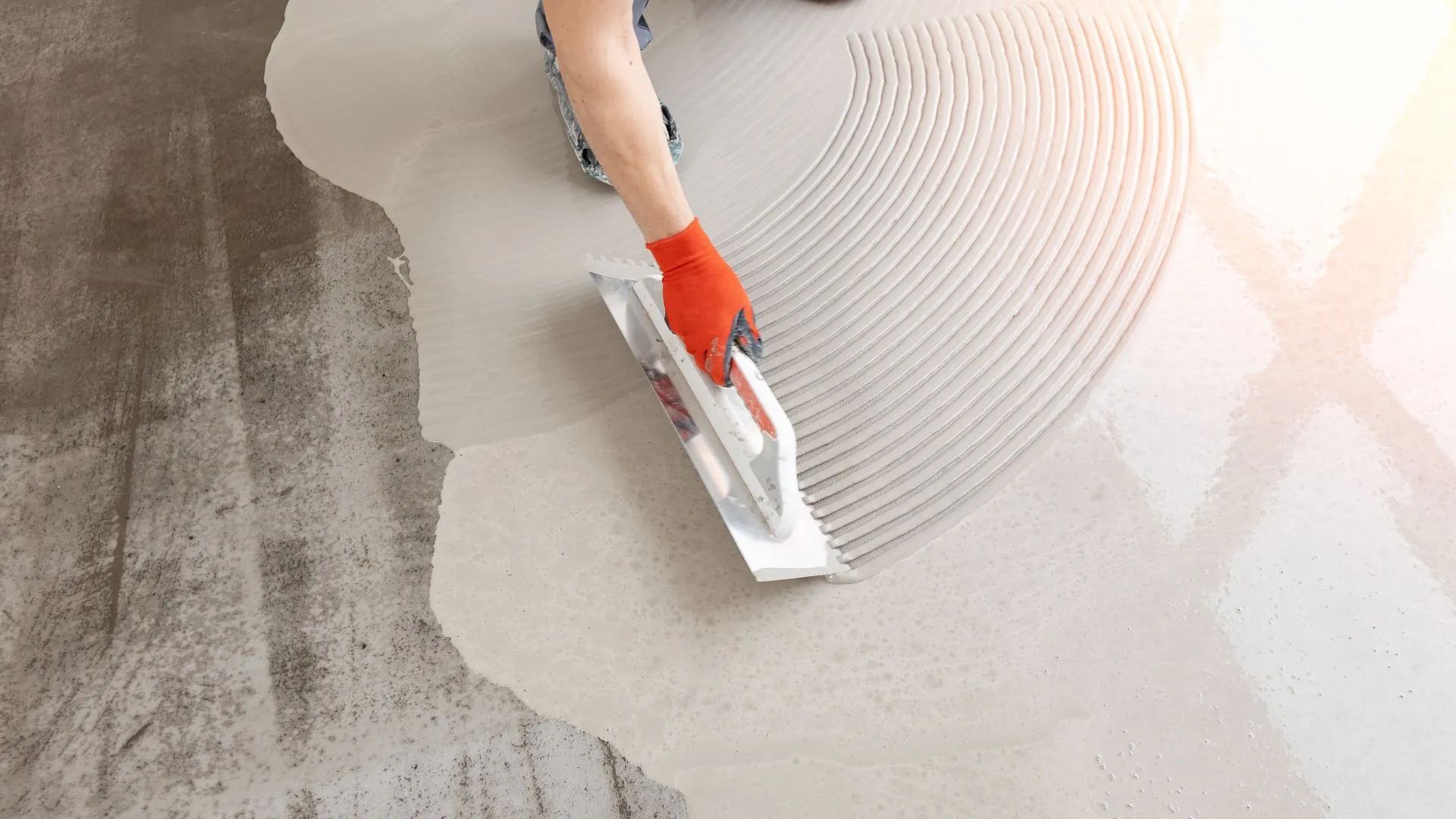 Person using a trowel to spread gray adhesive on a floor surface