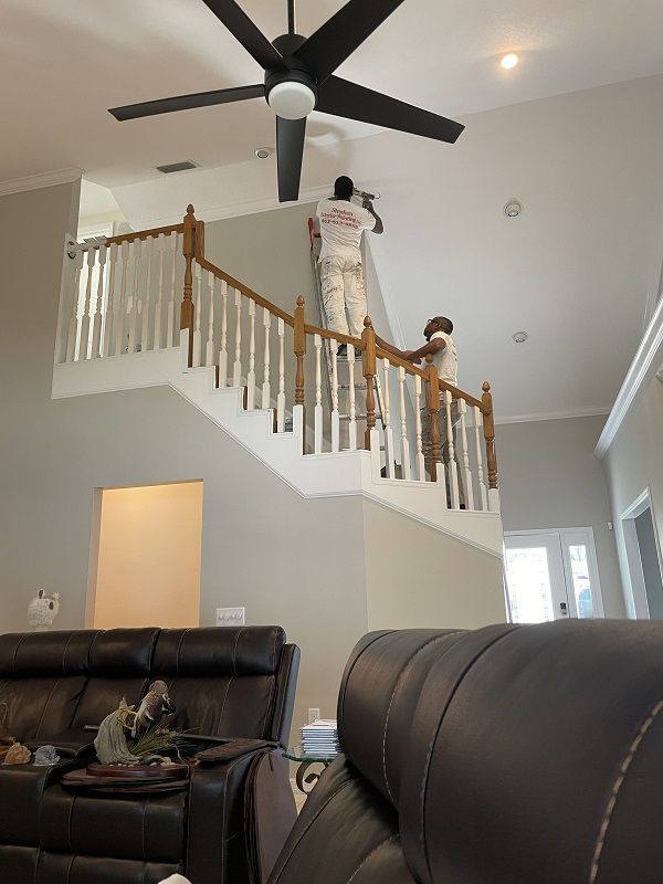 Person working on staircase railing in a living room with a high ceiling and ceiling fan.